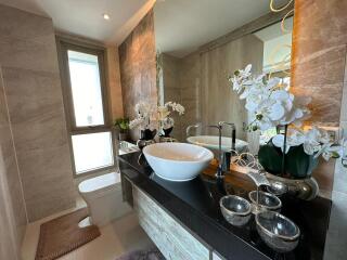 Modern bathroom with marble tiles, bowl sink, and decorative orchids