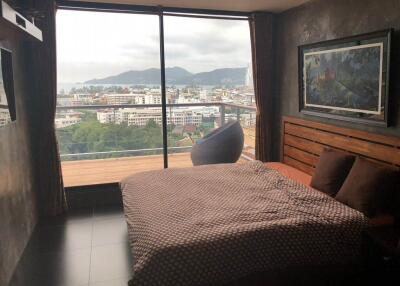 Bedroom with a large window, mountain and city view, bed, and cozy chair