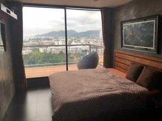 Bedroom with a large window, mountain and city view, bed, and cozy chair