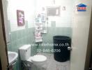 Clean bathroom with green tiles, toilet, shower, and a large black storage bucket