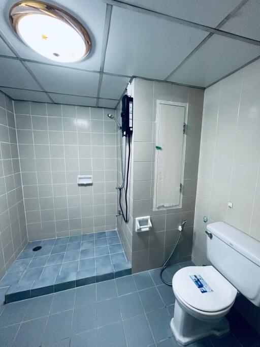 Bathroom with tiled walls and floor, featuring a shower area and a toilet
