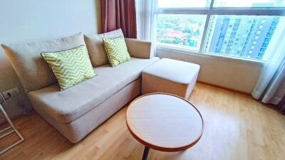 Bright living room with a sofa, ottoman, and coffee table near a large window with city views