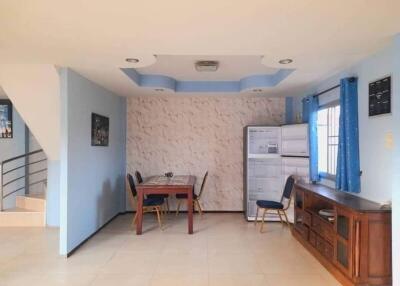 Dining area with a wooden table and chairs, refrigerator, and window with blue curtains.