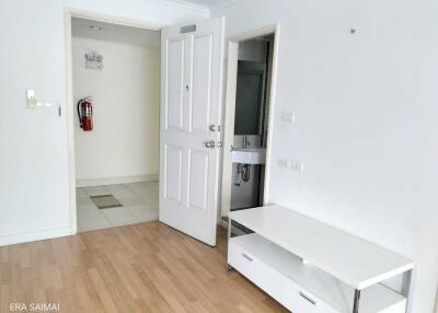 Living area with wooden floor, white walls, a door, and a small white media console