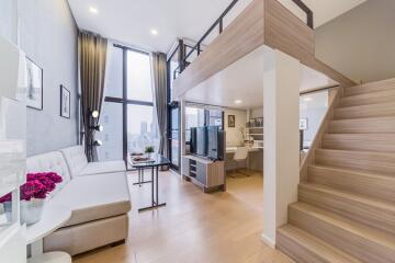 Modern living area with large windows, a sectional sofa, TV, and a loft space