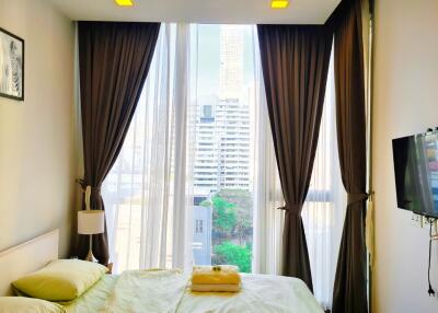 A cozy bedroom with a modern design, featuring large windows with city view.