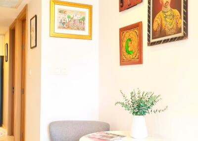 Brightly lit corner with a small chair and table, decorated with framed art and green plants