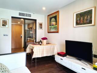 A cozy living room with a television, small dining area, and kitchen entrance