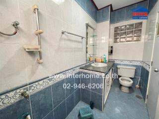Modern bathroom with blue and white tiles, a countertop with toiletries, a toilet, and a shower area
