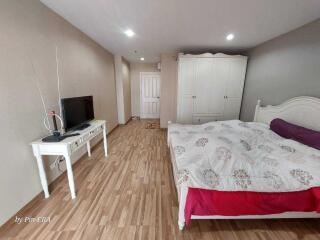 Modern bedroom with wooden flooring, TV, and white wardrobe