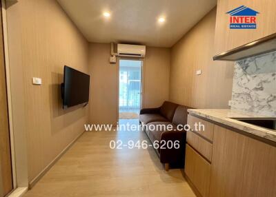 Cozy living room with a sofa, wall-mounted TV, air conditioning unit, and a kitchenette with marble countertops.