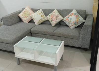 Living room with grey L-shaped sofa, decorative pillows, and glass-top coffee table