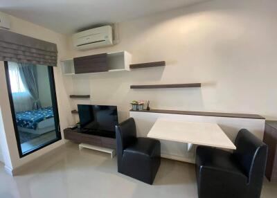 Modern living room with a TV, desk and chairs, and a sliding door to the bedroom