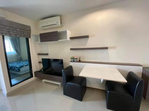 Modern living room with a TV, desk and chairs, and a sliding door to the bedroom