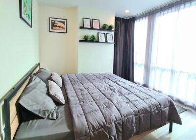A spacious bedroom with a double bed, framed pictures on the wall, and large windows with curtains