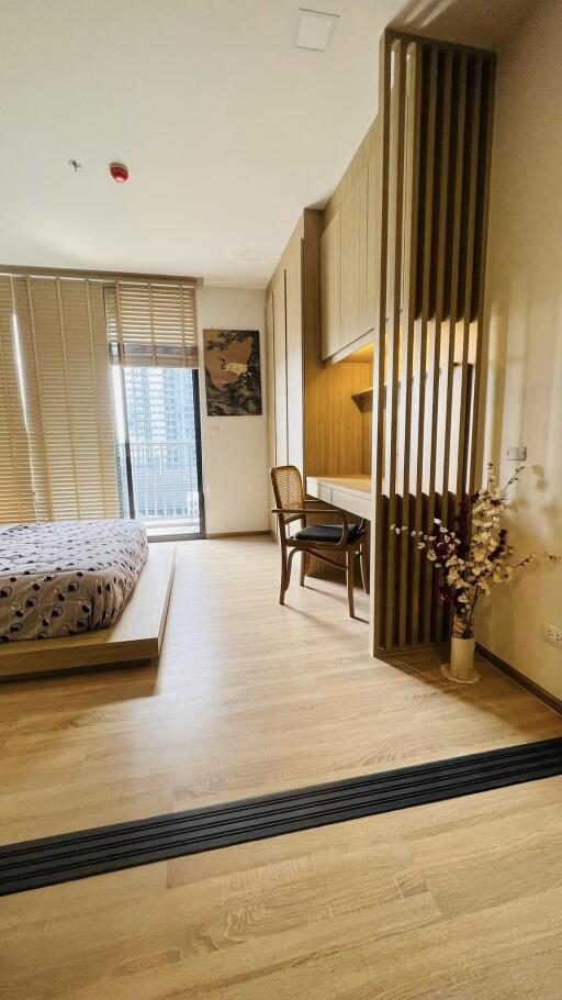 Modern bedroom with wooden flooring, a bed, a work desk, and large windows with blinds