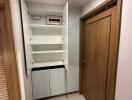 Utility closet with open cabinet doors showcasing shelves and an electrical panel