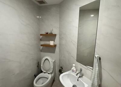 Small modern bathroom with toilet, sink, mirror, and shelves