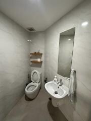 Small modern bathroom with toilet, sink, mirror, and shelves