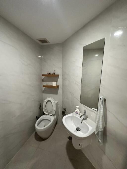 Small modern bathroom with toilet, sink, mirror, and shelves