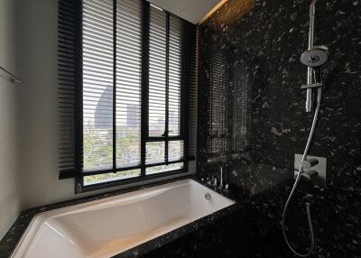 Luxurious bathroom with bathtub and shower, featuring black marble walls and large window with blinds.