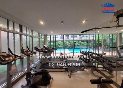 Fitness room with various exercise equipment and large windows showing a pool view
