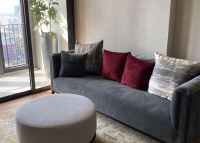 Living room with grey couch, colorful pillows, round ottoman, and large windows with city view