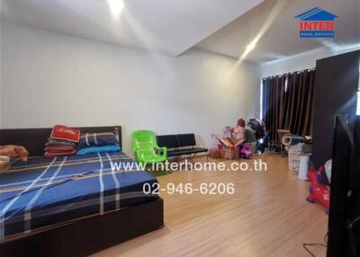 A bedroom with wooden flooring, bed with checkered linens, green chair, and assorted furniture and items.