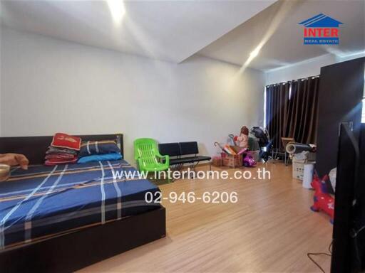 A bedroom with wooden flooring, bed with checkered linens, green chair, and assorted furniture and items.