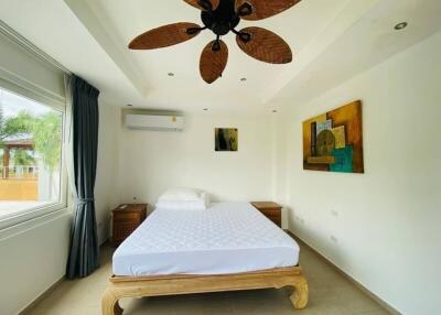 A bright and spacious bedroom with a bed, side tables, wall art, and a ceiling fan.