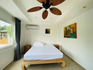 A bright and spacious bedroom with a bed, side tables, wall art, and a ceiling fan.