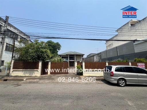 Exterior view of a residential building with a wooden fence and parked cars