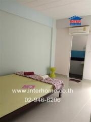 Simple bedroom with single bed, neutral wall colors, air conditioner, and a small green stool.