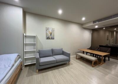 Modern living room with grey sofa, dining table, and a bed