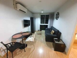 Modern living room with black leather sofa, wall-mounted TV, and dining table