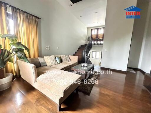 Modern living room area with a sectional sofa, decorative pillows, potted plant, and staircase leading to upper level