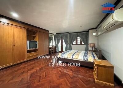 Spacious bedroom with wooden flooring, large bed, built-in closet, air conditioning, and large windows with drapes.