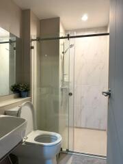Modern bathroom with toilet, sink, glass shower enclosure, and potted plant