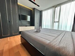 Modern bedroom with wooden flooring, large windows, and a mounted TV