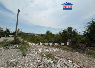 Vacant land with scattered debris and greenery in the background