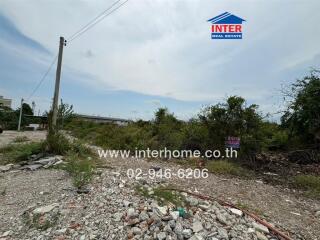 Vacant land with scattered debris and greenery in the background