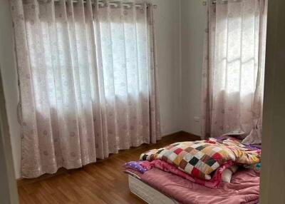 Bedroom with wooden floor, two windows with curtains, and bed