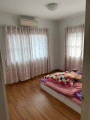 Bedroom with wooden floor, two windows with curtains, and bed