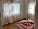 Bedroom with wooden floor, two windows with curtains, and bed