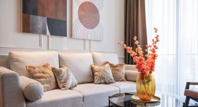 Modern living room with a beige sofa, decorative pillows, abstract wall art, and a glass coffee table with a floral arrangement