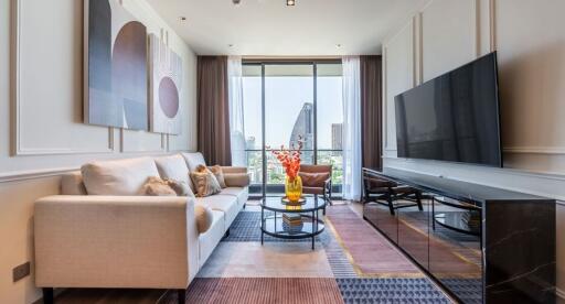 Modern living room with a large TV, contemporary furniture, and a view of city buildings through large windows.