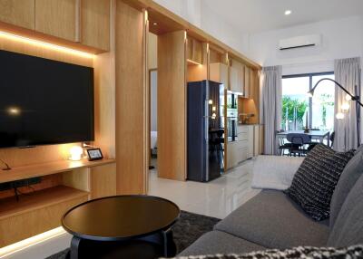 Modern living area with built-in wooden cabinetry, large flat screen TV, and view into the kitchen and dining area