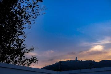 View from a property balcony featuring a scenic landscape with a mountain and a statue at sunset