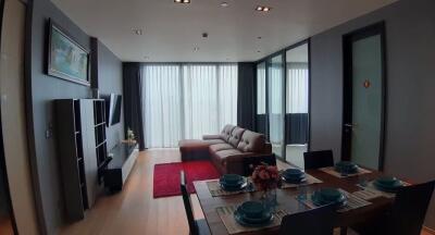 Modern living and dining area with large windows, sofa, TV, and dining table