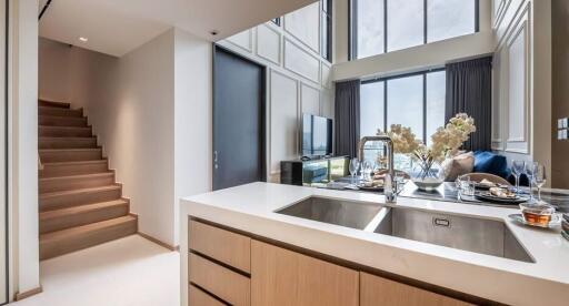 Modern kitchen with a view of the living area featuring a high ceiling and large windows.